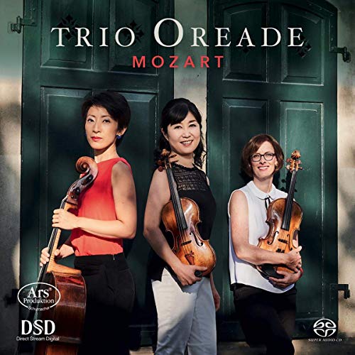 Three women holding string instruments stand before a green double door.