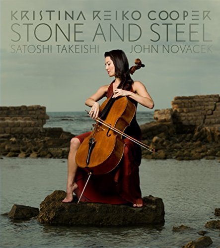 Woman in red dress plays cello on a rock in shallow water.