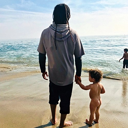 A man with dreadlocks holds a naked child on a beach with another child.