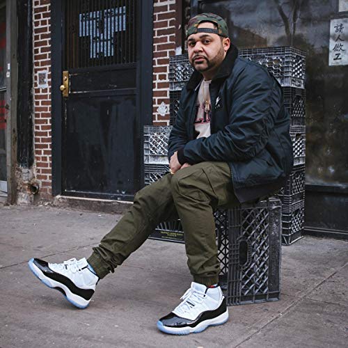 Man sitting on crate wearing black jacket, olive pants, and white sneakers with black accents.