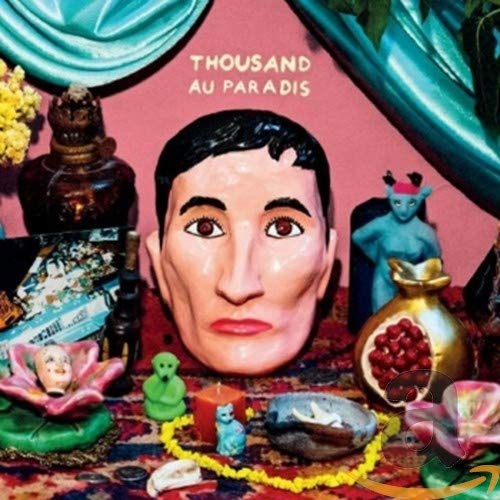 "Album cover with a large doll's head surrounded by various objects on a colorful rug."
