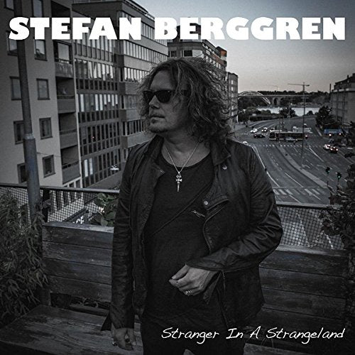"Album cover with a man in dark clothing standing by a cityscape."