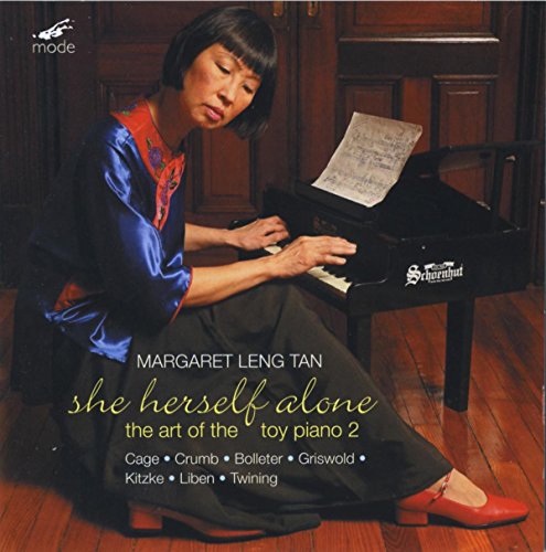 Woman in blue dress playing toy piano with sheet music on a wooden floor.