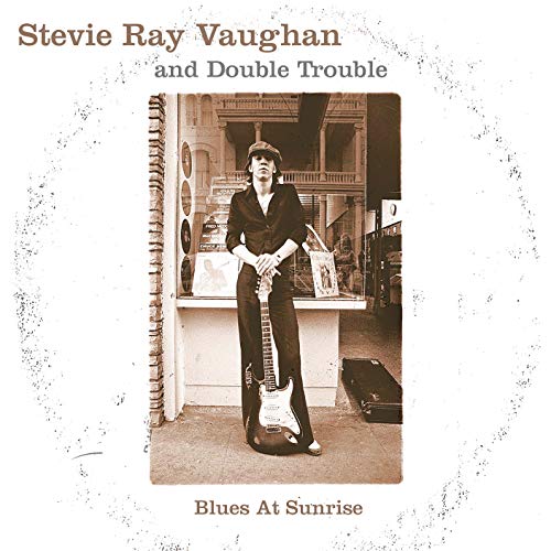 Album cover with a man holding a guitar in front of a shop.