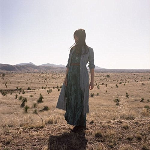 A woman in a long, green dress stands in a dry, open field.