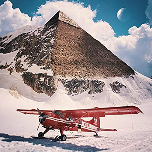"Red airplane on snowy ground in front of a large, rocky mountain."