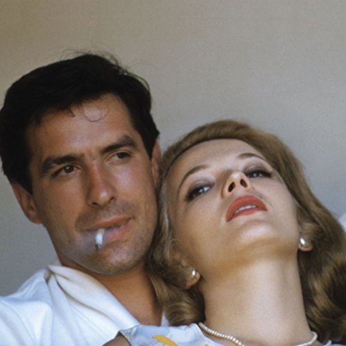 "Man and woman leaning heads together, man smoking, against a plain beige background."