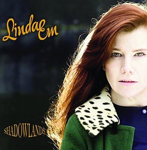 A woman with long red hair and a green coat on a dark album cover.