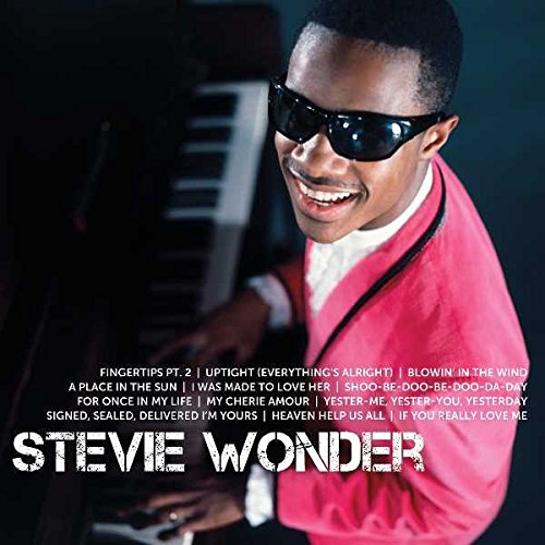 Stevie Wonder in a pink jacket, smiling, with a keyboard behind him.
