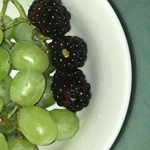 The image is unrelated to the product information. A suitable alt text for the image is: "A white bowl containing green grapes and blackberries on a green surface."