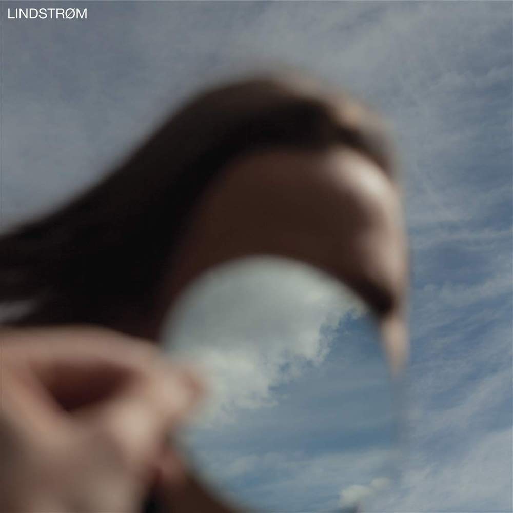 A hand holds a reflective disc showing a cloudy blue sky.
