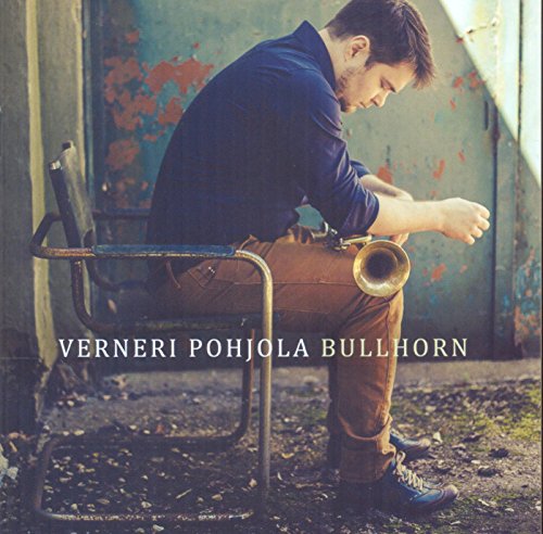 Man sitting on a metal chair, holding a trumpet, in front of a grungy wall.
