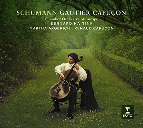 A man plays cello in a serene, grassy path surrounded by trees and hedges.