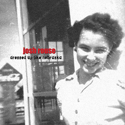 Black and white album cover with a man smiling in front of a building.
