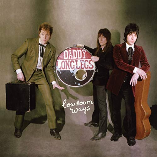 "Album cover featuring three men in suits posing with a drum and guitar case."