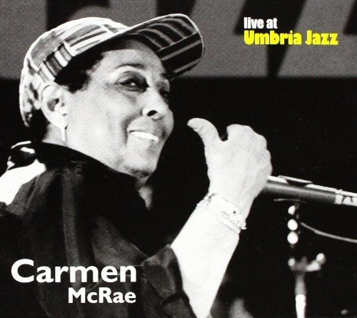 The image is a black and white photograph of Carmen McRae, a renowned jazz singer, captured in a moment of performance. She is depicted wearing a cap and holding a microphone, with her name prominently displayed. The image is accompanied by the text "live at Umbria Jazz" in the top-right corner. Alt text: Black and white image of Carmen McRae singing into a microphone.