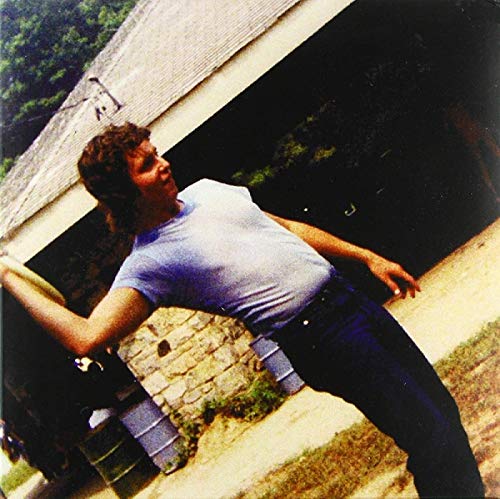 The alt text for the image is: "Man leaning against a covered bridge, wearing a white t-shirt."