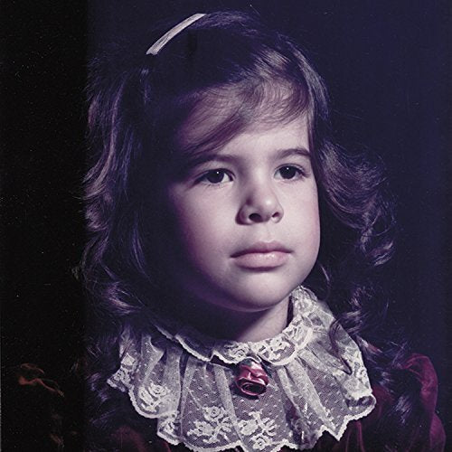 Young girl with curly hair and lace collar against a dark background.