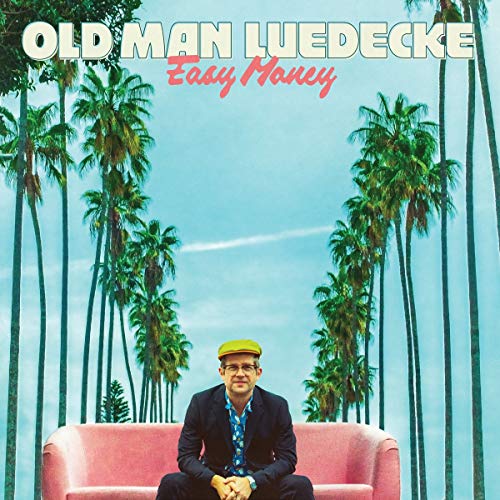 Album cover with man sitting on pink couch, surrounded by palm trees.
