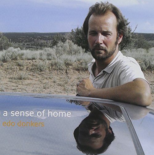 A man leans on a car in a desert landscape, CD album cover.