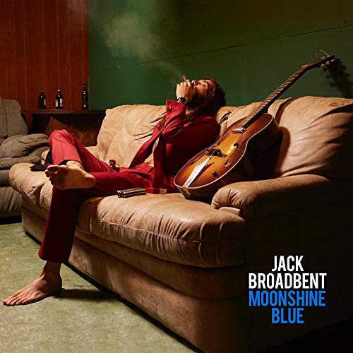 "Album cover with man in red lounging on couch with guitar, smoking."