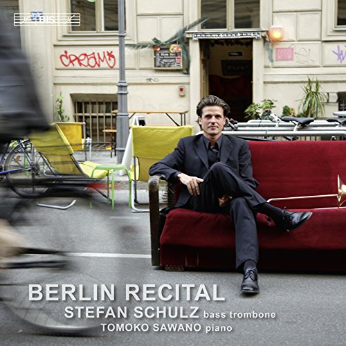 Man in a suit sits on a red sofa on a city street.