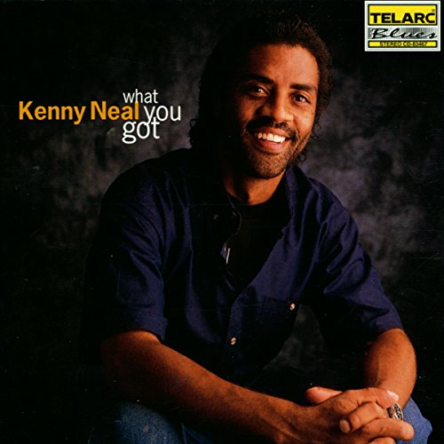 Kenny Neal's album cover featuring the artist sitting with a dark background and text overlay.