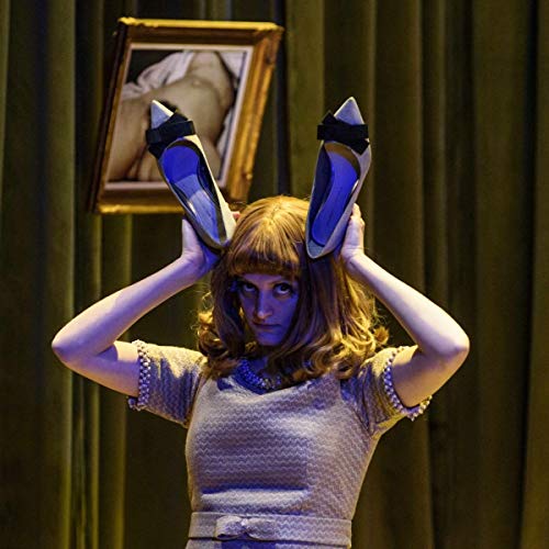 A woman holds shoes above her head against a green curtain backdrop.