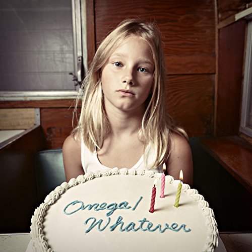 Young girl with blonde hair sits behind a cake with "Omega/Whatever" written on it.