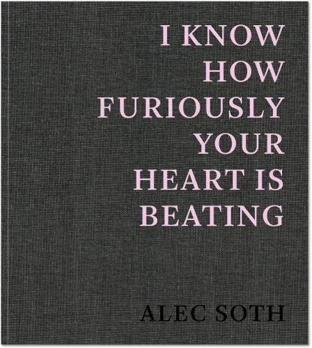 The image depicts a book cover with the title "I Know How Furiously Your Heart Is Beating" by Alec Soth. The cover is gray, featuring pink text that reads: "I KNOW HOW FURIOUSLY YOUR HEART IS BEATING" in a stacked format, with the author's name "ALEC SOTH" printed in black at the bottom. Alt text: Gray book cover with pink text reading "I Know How Furiously Your Heart Is Beating" by Alec Soth
