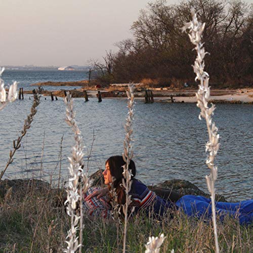 The alt text for the image is: "Woman lying on a rocky shore with a body of water."