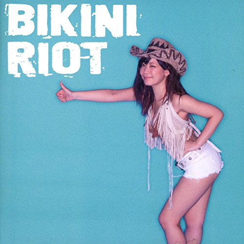 Woman in white bikini top and shorts, cowboy hat, against turquoise background, thumbs up.