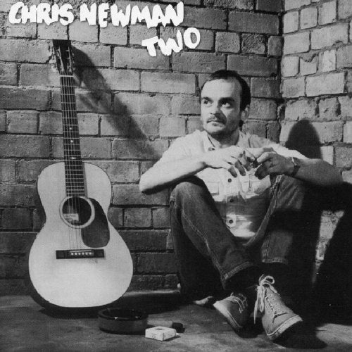 Black and white album cover with man sitting by a guitar against a brick wall.