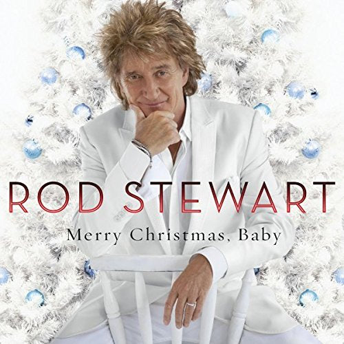 Rod Stewart in white, leaning on a chair, surrounded by a white Christmas tree.
