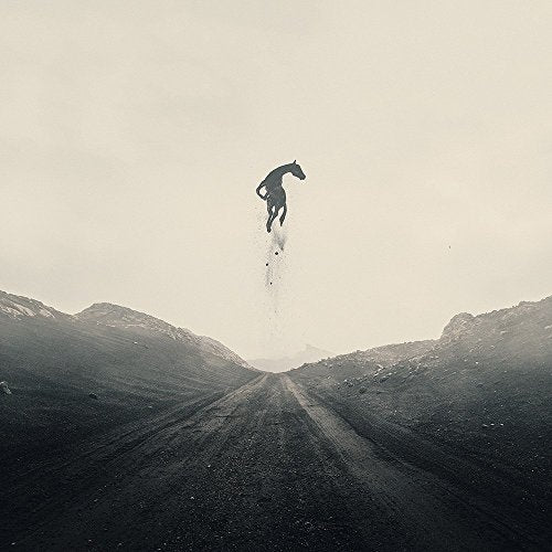 A black-and-white image of a horse jumping over a dirt road between mountains.