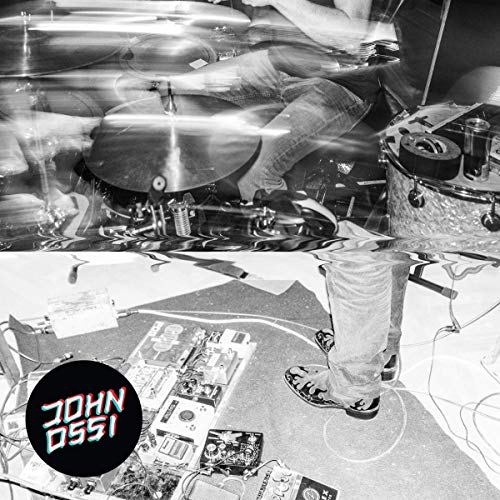 A monochrome image showing a drum set in motion, with the words 'Johnossi' written on the bottom left.
