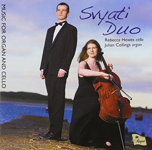 A man and woman in formal attire stand on a rocky shore with a cello.