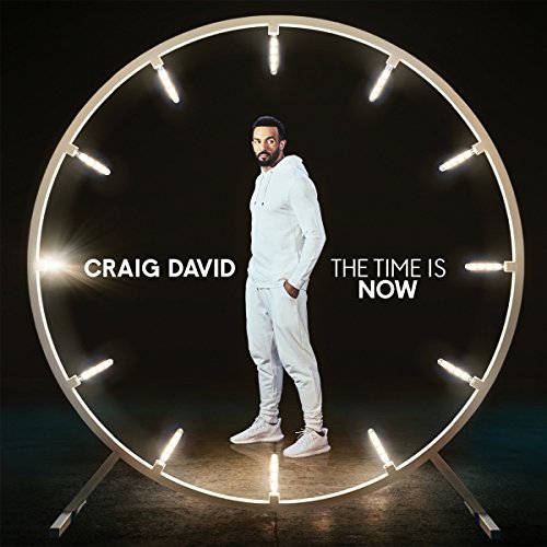 Craig David stands in a lit circular frame, wearing white, against a dark background.