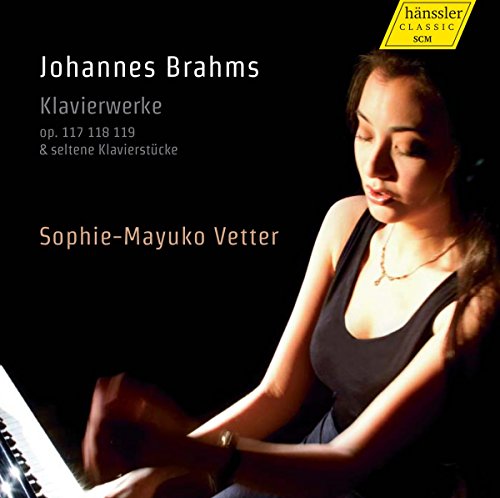 A woman plays piano, wearing a black tank top, against a dark background.