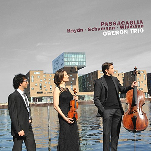 "CD cover featuring three musicians standing by water with modern buildings in the background."