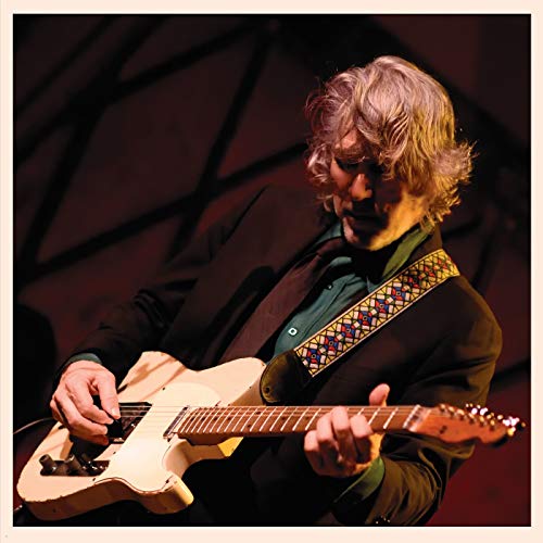 A man playing a cream-colored electric guitar on stage with a patterned guitar strap.