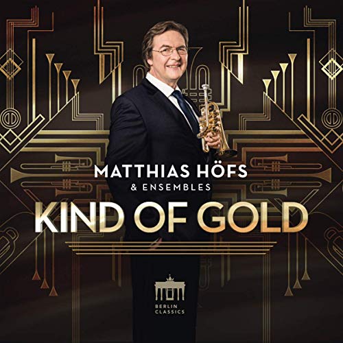 Man in a suit holding a trumpet, against a dark background with gold designs.