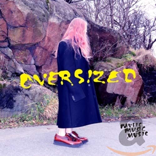A woman with pink hair stands before rocks, with "OVERSIZED" written across in yellow.