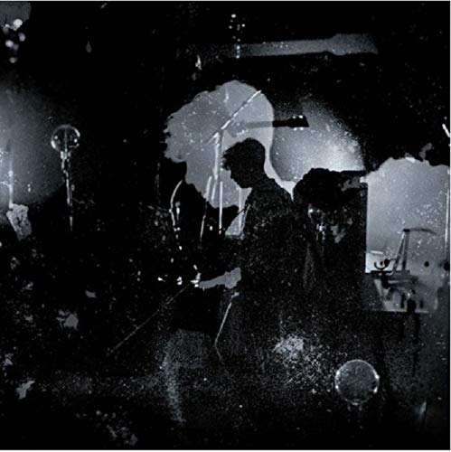 Black and white image of musicians on stage, silhouetted against a bright background.