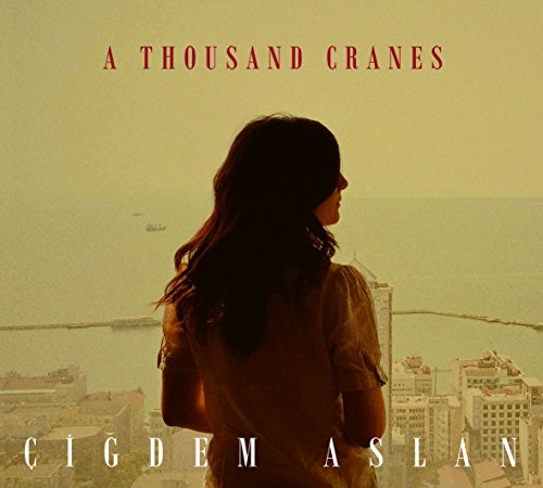 A woman with long dark hair looks out over a cityscape on a CD cover.
