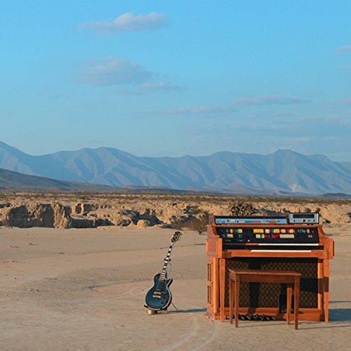 The image shows a guitar and piano in a desert landscape. "Vinyl record album cover with desert scene, guitar, and piano."