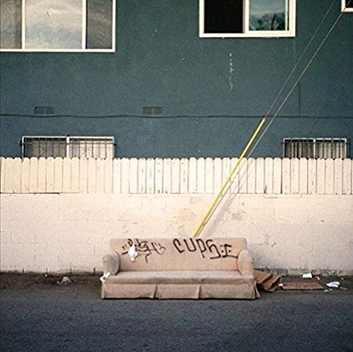 A vinyl record cover featuring a graffiti-tagged couch outside a building with a white picket fence.