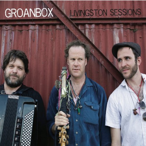 "Album cover featuring three men standing in front of a red metal wall."