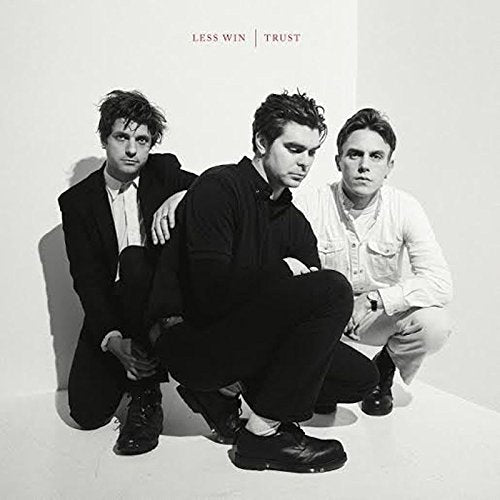 "Three men crouching against a white wall, dressed in dark and light attire."