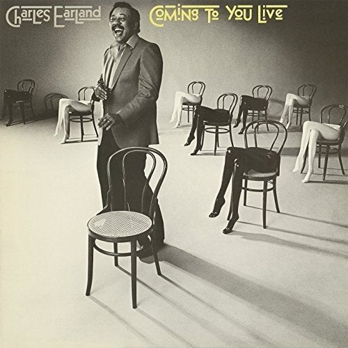 "Black and white album cover with man standing, surrounded by empty chairs."